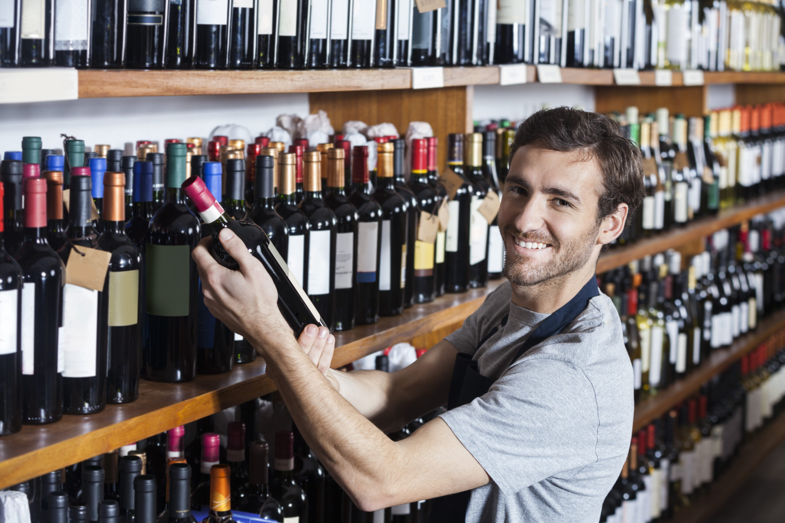 Portrait of smiling salesman arranging wine bottle on shelf in shop